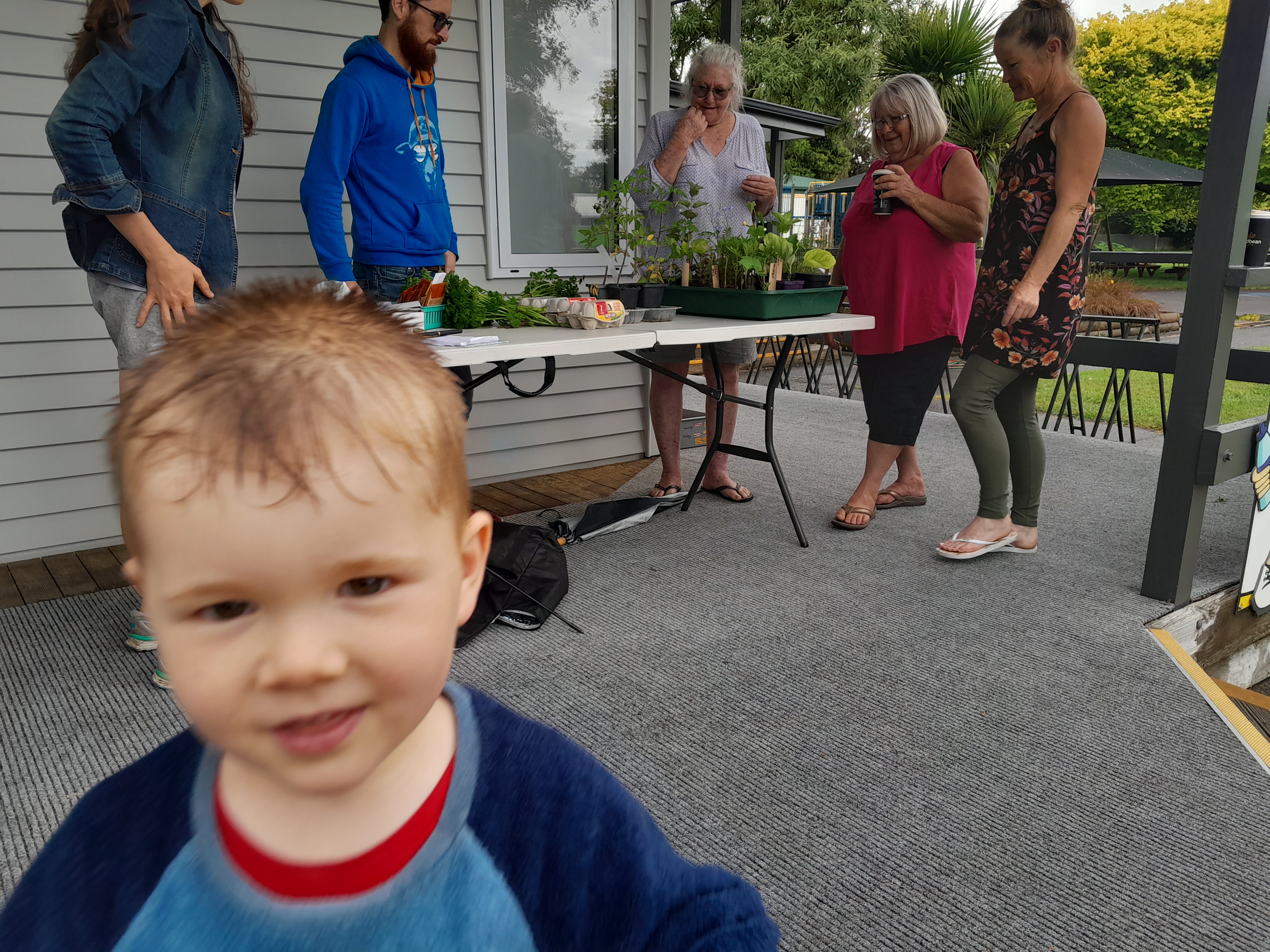 Produce lined up on table surrounded by swappers, photobombed by young boy.